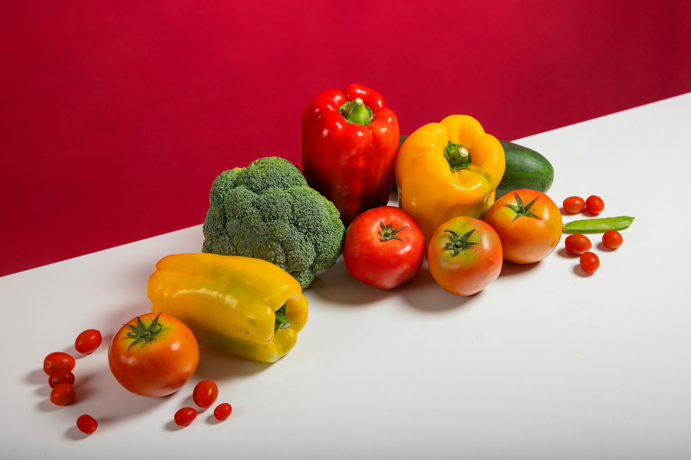Verse groente en fruit op een rode achtergrond — paprika's, broccoli, tomaten