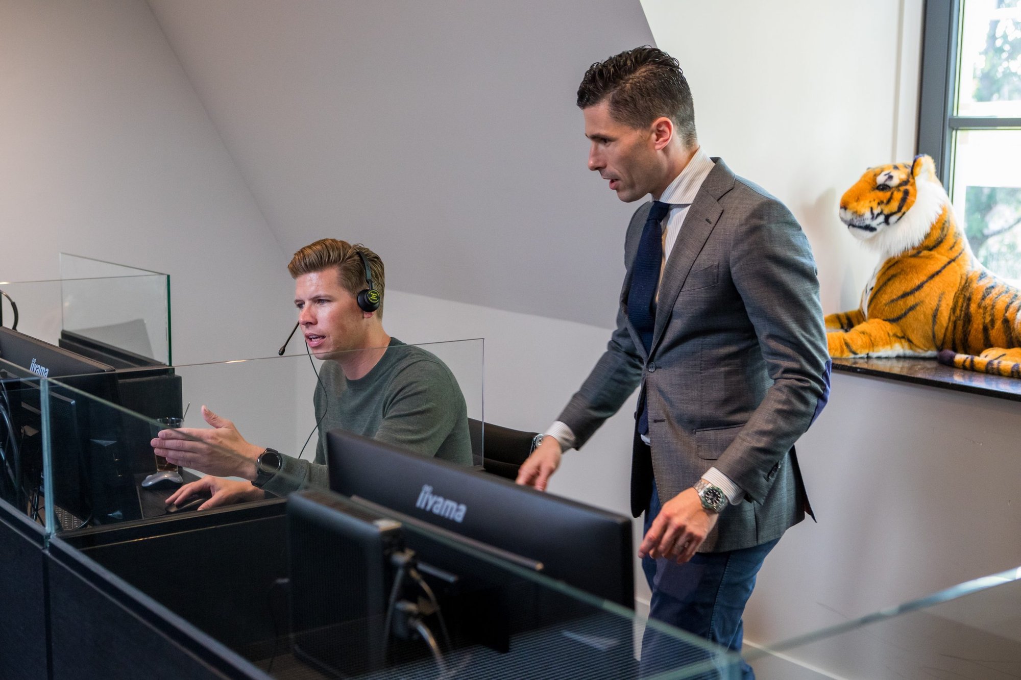 Salescoach naast een accountmanager achter zijn scherm — coaching-moment op de werkvloer