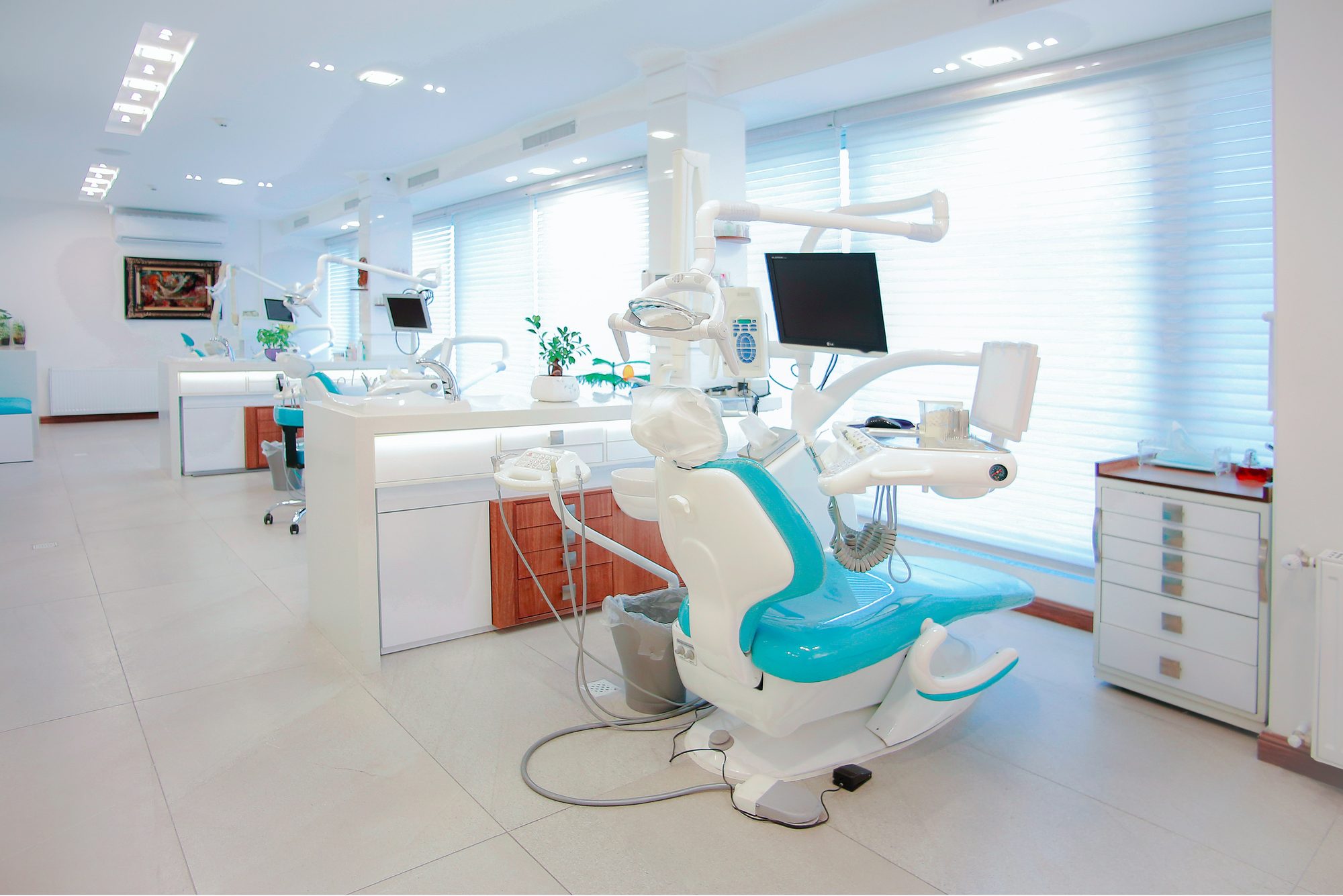 Ruime, moderne tandartsclinic met turquoise behandelstoel en witte inrichting