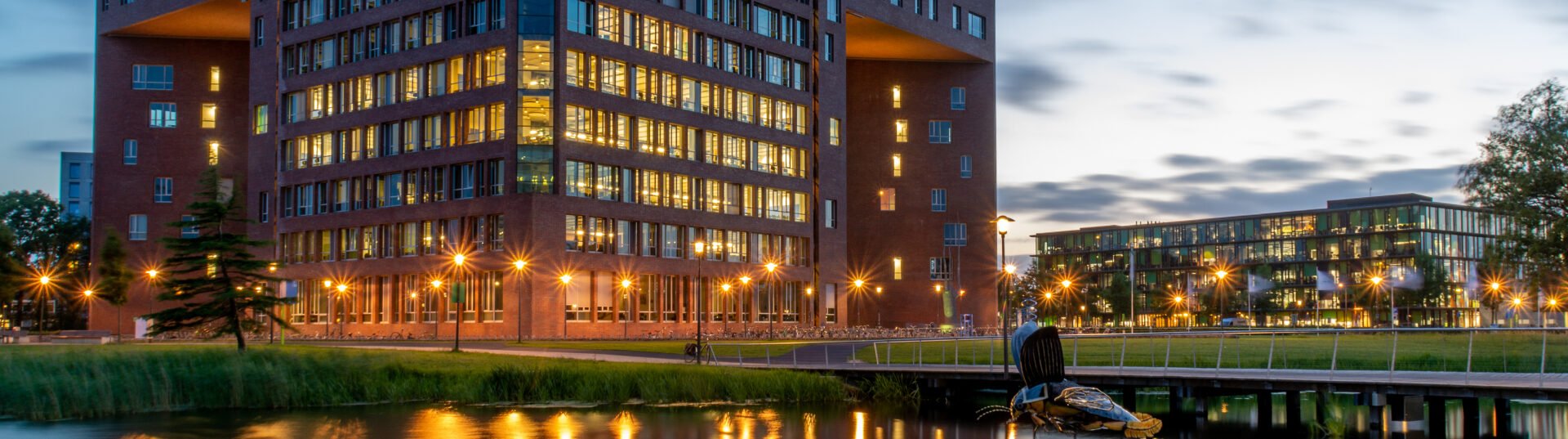 Wageningen University & Research campus bij avond, met het verlichte Atlas-gebouw gereflecteerd in het water