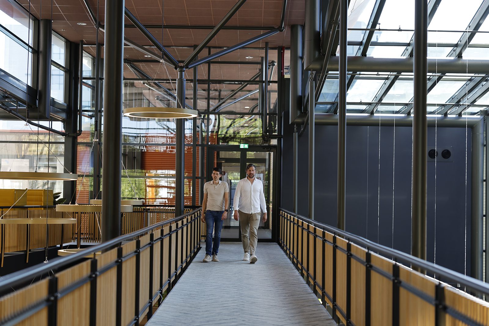Twee Emendis-collega's lopen door de loopbrug van het kantoor